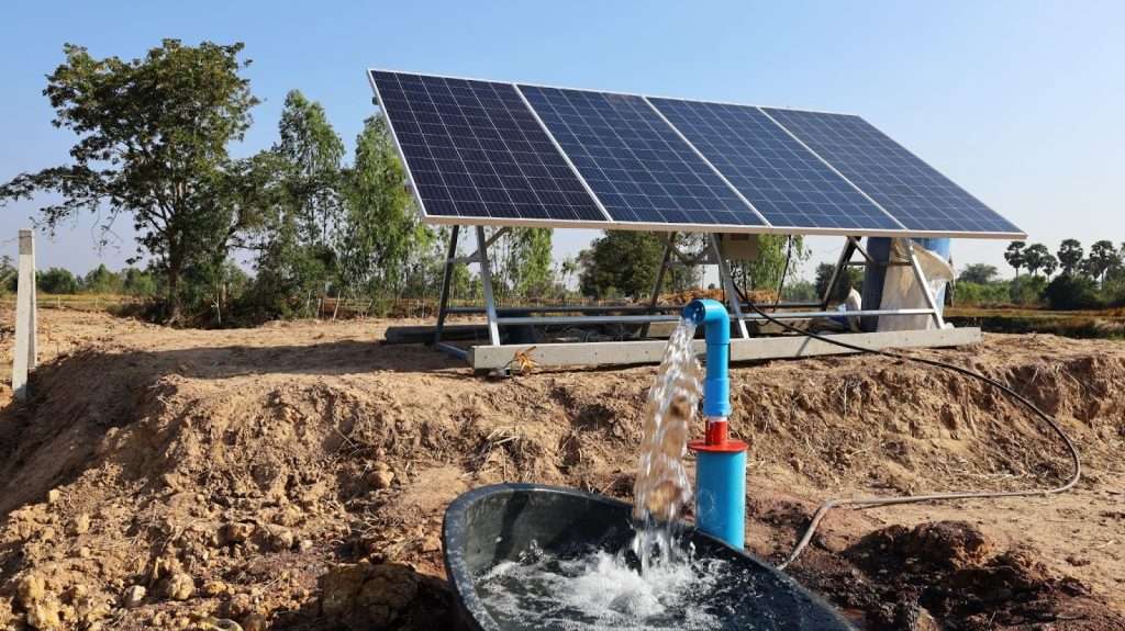 Image of a solar-powered water pump operating efficiently on agricultural land. Large solar panels mounted on a frame harness sunlight to power the pump, which delivers water into a trough. This setup demonstrates the cost-effective and environmentally friendly benefits of solar energy for agricultural water needs, particularly in remote locations, as highlighted in the Verendrye Electric Cooperative case study